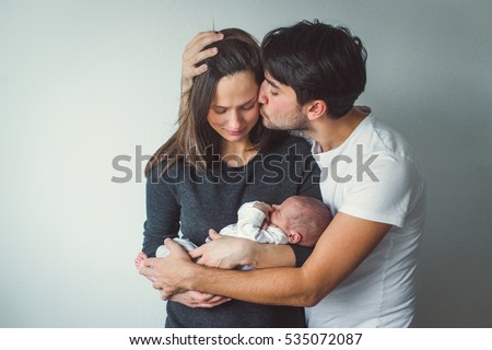Woman and man holding a newborn.  A man kisses a woman. Royalty-Free Stock Photo #535072087