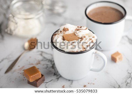 Hot chocolate with salted caramel and whipped cream in white vintage cups on the marble table.