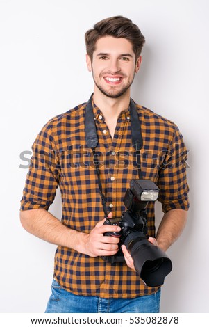 Portrait of young handsome cheerful photographer holding camera