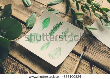 Watercolor painting with leaves on wooden table