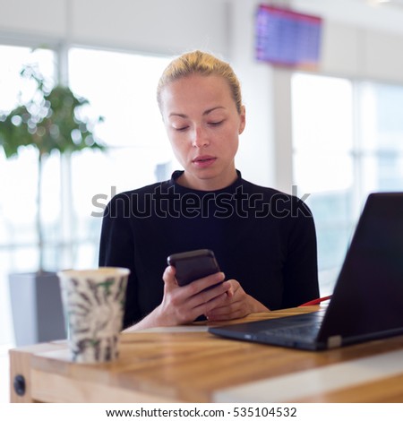 Female freelancer remotely working on the go using multiple devices on a desk at airport coffee shop while traveling. Contemporary entrepreneurial lifestyle.