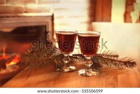 Glasses of mulled wine and coniferous branch on wooden table against blurred fireplace