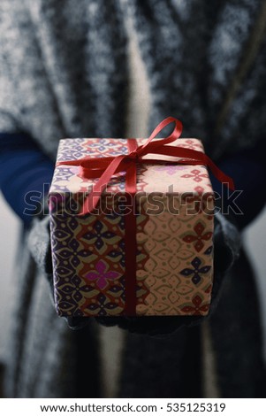 closeup of a young caucasian woman holding a cozy gift tied with red ribbon in her hands