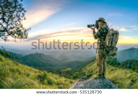 Blur Young man with backpack taking a photo on the top of mountains, sunset