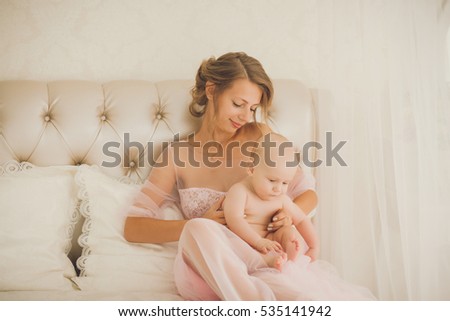 Mother and child on a white bed. Mom and little kid relaxing at home. Family having fun together. Bedding and textile for infant nursery.