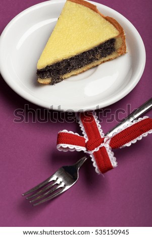 single slice of pie with poppy seeds on white plate near silver fork with festive red bow on purple background, side view