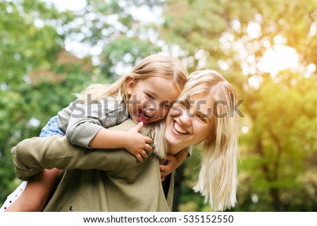 Cute young daughter on a piggy back ride with her mother. Royalty-Free Stock Photo #535152550