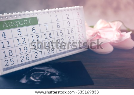 Calendar with ultrasound scan of baby and children shoes on wooden table