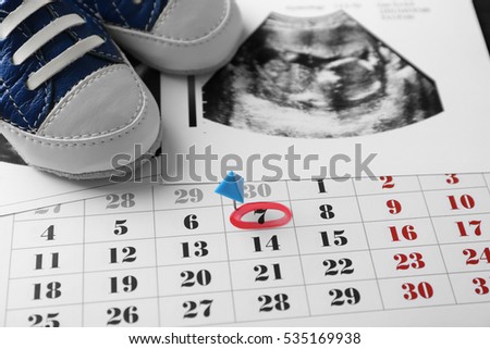 Calendar with ultrasound scan of baby and children shoes, closeup