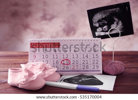 Calendar with mark, ultrasound picture of baby and children shoes on table