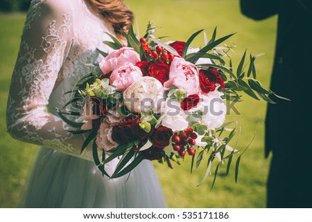 bride in a white dress holding a bouquet of flowers and greenery on the background of green grass
