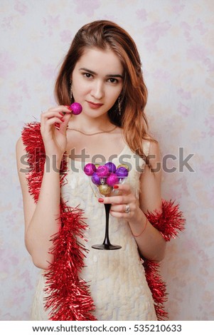 New 2017 Year is coming! Picture of joyful young woman in a brilliant dress and red tinsel having fun. Look at camera. Christmas spirit. Tricky Girl is holding martini glass and bites Christmas toy.