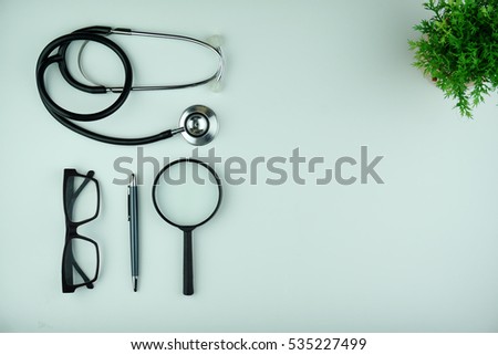 Top view of white office desk table with stethoscope, smartphone, notebook, spectacle, pen and magnifying glass. Flat lay and copy space.
