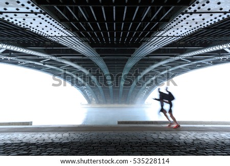 Anonymous male athletes running under a bridge in Lyon on a foggy winter day. Sports concept with motion blur and shallow focus.