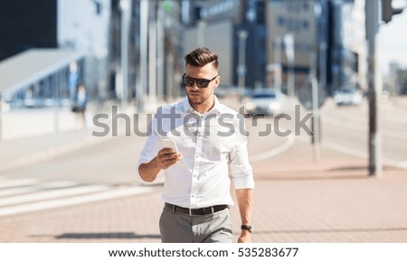 business, technology, communication and people concept - young man in sunglasses with smartphone walking in city Royalty-Free Stock Photo #535283677