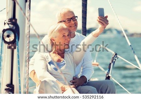 sailing, age, tourism, travel and people concept - happy senior couple taking selfie with smartphone on sail boat or yacht deck floating in sea