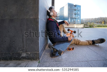 Skateboarder sitting in urban area listening to music