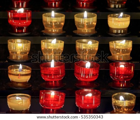 series of lit votive candles placed inside small colored glass glasses of red and yellow shooted in the church of st. jakob in the Austrian town of Villach