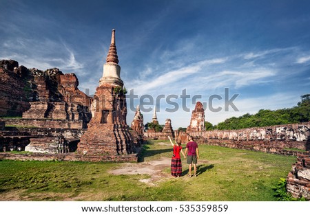 Young Couple in red clothes with photo camera looking at ancient ruined Wat Mahathat in Ayutthaya, Thailand
