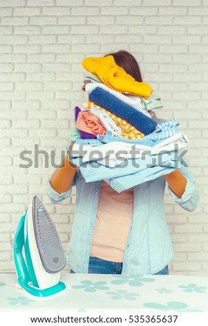 Housewife bringing a huge pile of laundry on the ironing board