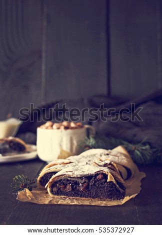 Slice of fresh baked homemade strudel with poppy seeds and  sugar powder,  on a black background  and fir branches. Cocoa with murshmelou. Christmas, winter still life