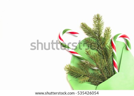 Cristmas composition. Green envelope, fir tree branch and candy canes on white background. Top view. Flat lay