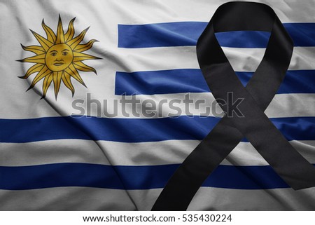 waving national flag of uruguay with black mourning ribbon