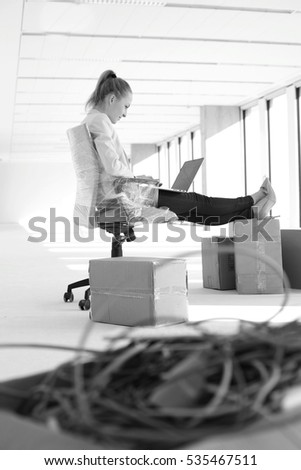 Side view of young businesswoman using laptop with feet up on cardboard box in office