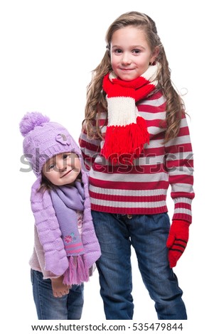 Cute smiling sisters wearing colorful knitted sweater, scarf, hat and gloves isolated on white background. Winter clothes.