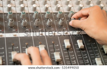working on sound desk adjusting levels,Hands working on a sound mixing desk in studio,radio host operating sound mixer on table at studio, Audio control buttons,hands turning up volume in radio studio