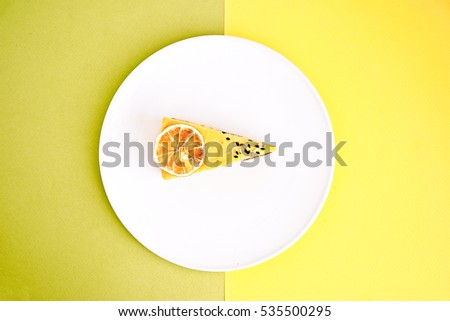Isolated piece of raw lemon and lime cake with dry lemon slice and sesame on top. Flat lay on a colorful yellow and light green background. Geometric style. Vegan, sugar, gluten, dairy free dessert.