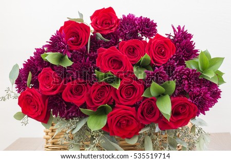 Red roses and dark pink flowers bouquet in wicker basket isolated on the white background