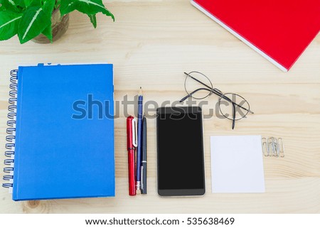 Smartphone, glasses, notebooks, pen, pencil, paper clips, green leaves pot on vintage wooden table