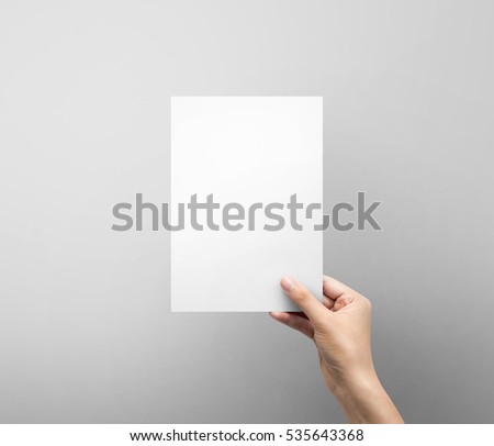Woman hand holding blank paper sheet A5 size or letter paper on grey background. Royalty-Free Stock Photo #535643368