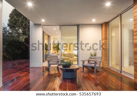 Wooden deck / balcony at night with furniture and open doors leading to inside. Royalty-Free Stock Photo #535657693