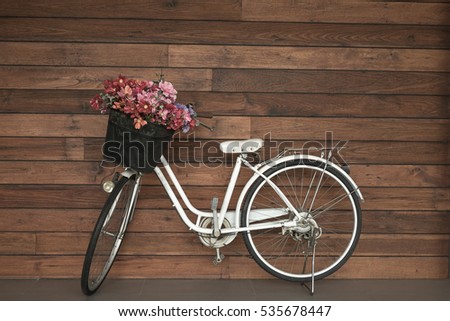 Image of white old and retro bicycle with flower basket leaning against wooden wall for sport or recreation background