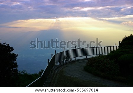 Mountain landscape with wave of fog, cloudy sky and metal fence near the path on the top of mountain with the view into misty valley. Doi Inthanon National Park, Chiang Mai, Thailand