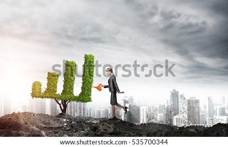 Young attractive businesswoman watering symbol chart plant in ground with can against the backdrop of the city