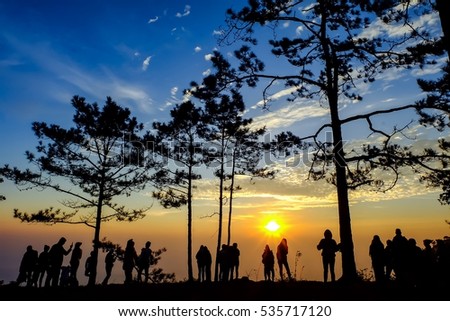 silhouette of trees and many people who wait for watch sunrise at cliff edge. This picture reflect to dramatic emotional and feel warm. Natural light is used. the sky is beautiful and colorful.