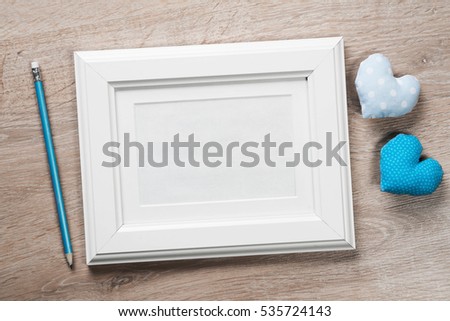 White photo frame small red hearts and pencil on wooden table