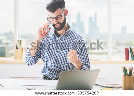 Handsome young boy at workplace talking on phone and showing fist, 'yes' gesture. Success concept 