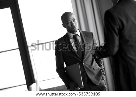 Young businessman holding file while listening to male colleague in office