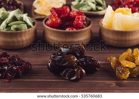 Assortment of dried fruits closeup on brown wooden background. Decorative border of dry exotic fruit in spoons, bowl. 