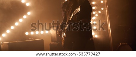 Electric guitar player on a stage with back scenic illumination, soft selective focus