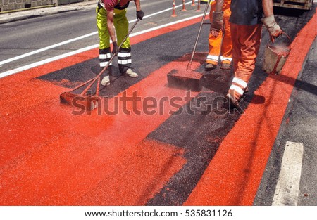 Road workers painting red color on the street surface 