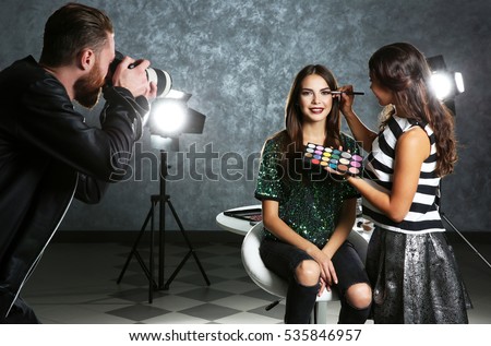 Professional makeup artist working with young beautiful woman at photo shooting