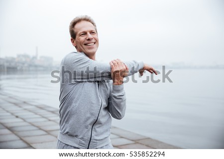Smiling Runner in gray sportswear warming up near the water