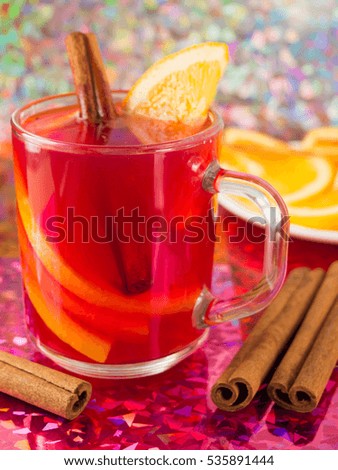Transparent mug with citrus mulled wine, cinnamon and orange to bright shiny background with blur and shallow depth of focus