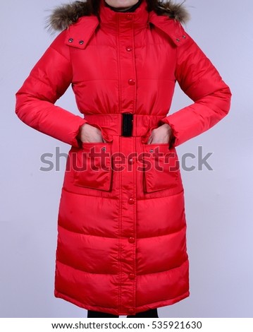 Winter down jacket with grey red collar isolated on a grey background. Fashionable red coat on model without face. Outerwear. 