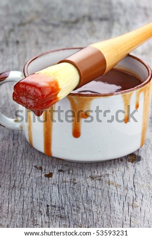 Basting brush drips tangy barbecue sauce onto a weathered wooden table. Shallow DOF.